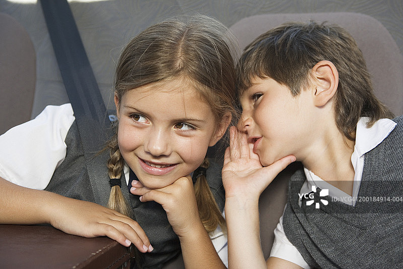 男孩(5-7)在女孩(5-7)的耳边低语，坐在车里，特写图片素材