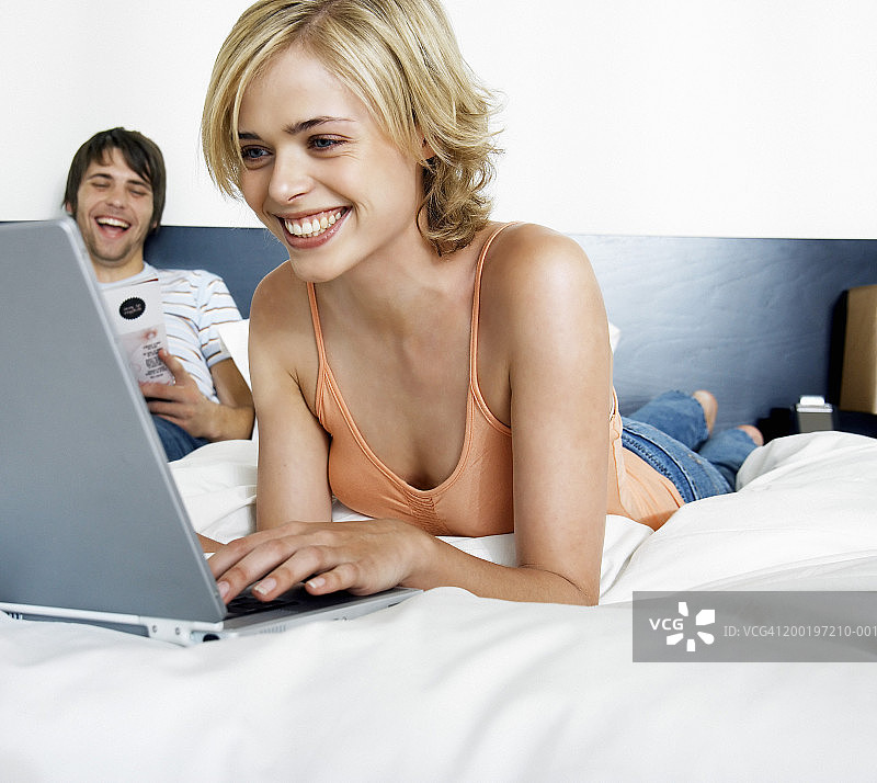 夫妇在床上，男人在看杂志(重点是女人在用笔记本电脑)图片素材