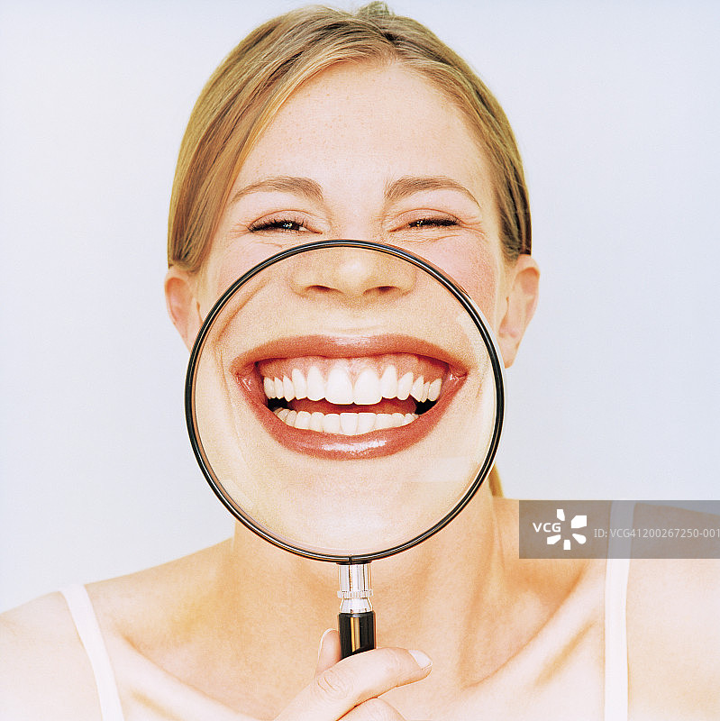 女人拿着放大镜在嘴边，微笑着，肖像图片素材