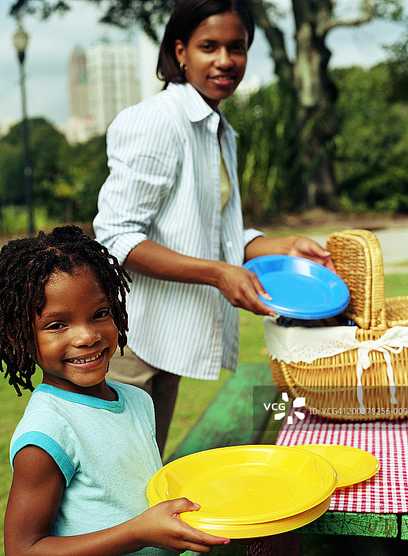 母亲和女儿(8-10)在野餐时摆好盘子图片素材