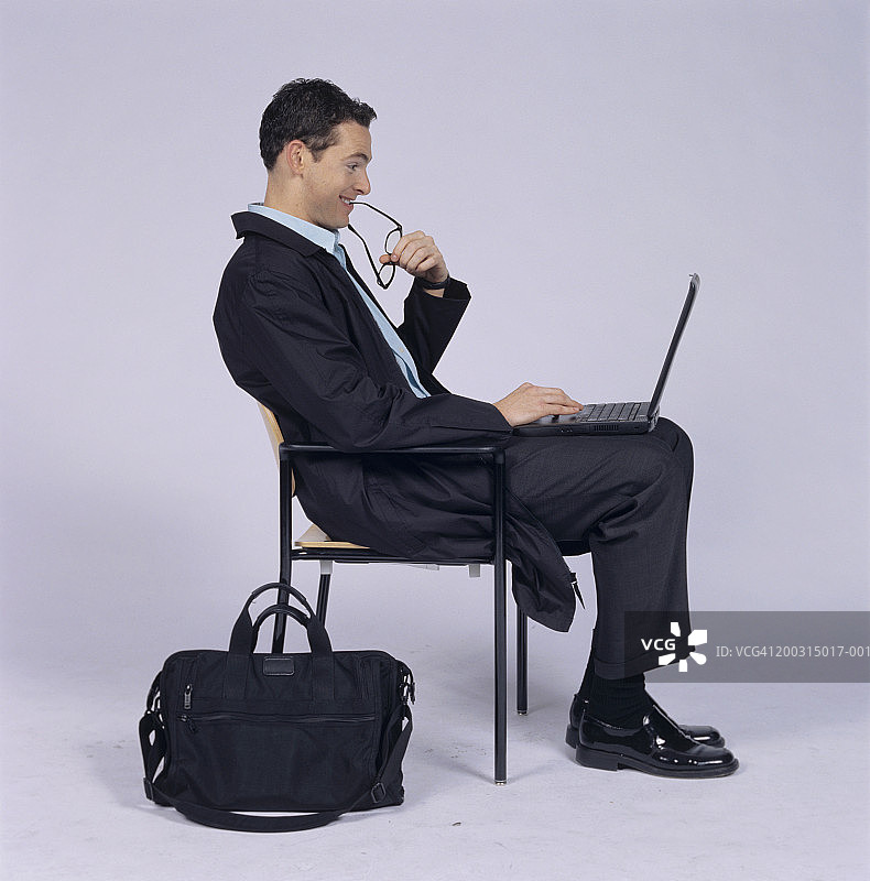 一名男子嚼着眼镜，坐下来，使用笔记本电脑图片素材