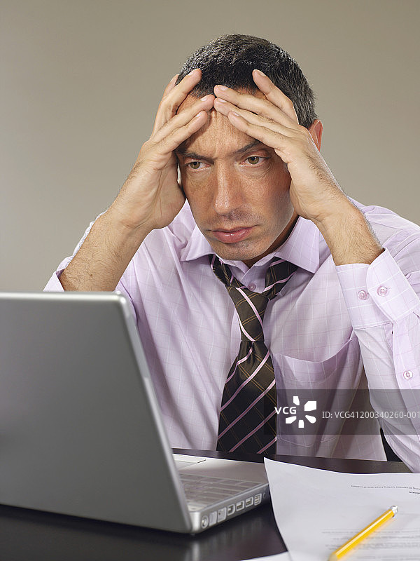 一名男子坐在笔记本电脑前，双手抱头，眉头紧锁图片素材