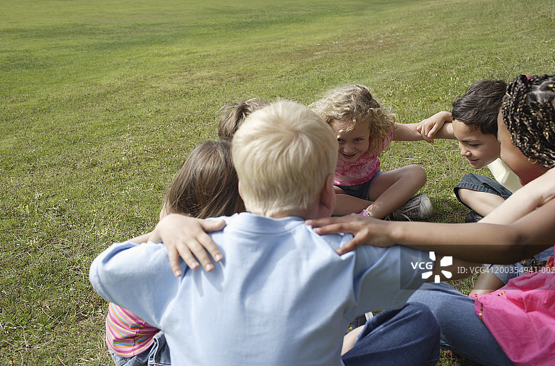 男孩和女孩(6-7岁)盘腿坐在草地上，手挽着手图片素材