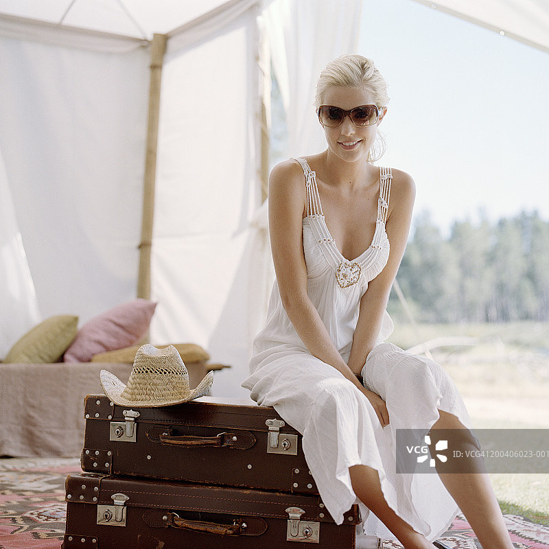 戴着墨镜的年轻女子坐在帐篷里的行李上图片素材