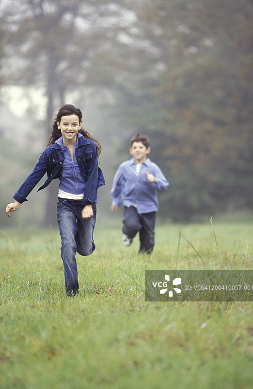 女孩和男孩(9-11)微笑着跑过田野图片素材
