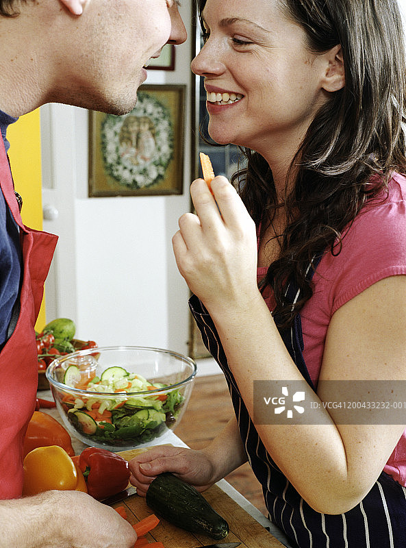 一对穿着围裙的夫妇在厨房里，互相微笑，特写镜头图片素材
