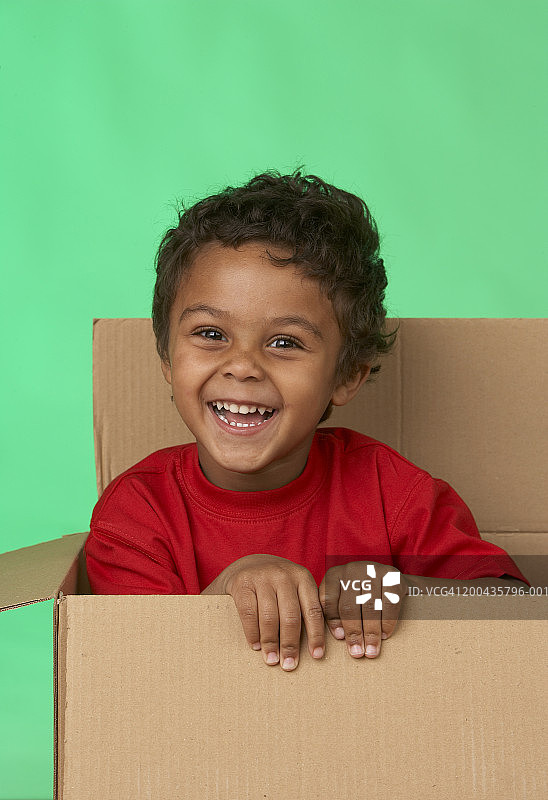 男孩(5-7岁)坐在纸板箱里，微笑着，肖像图片素材