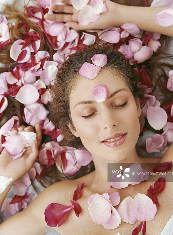年轻女子躺下，满身玫瑰花瓣，面带微笑，俯视图片素材