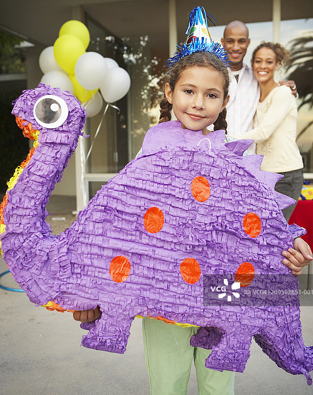 女孩(8-10)在生日聚会上拿着紫色的恐龙皮纳塔图片素材