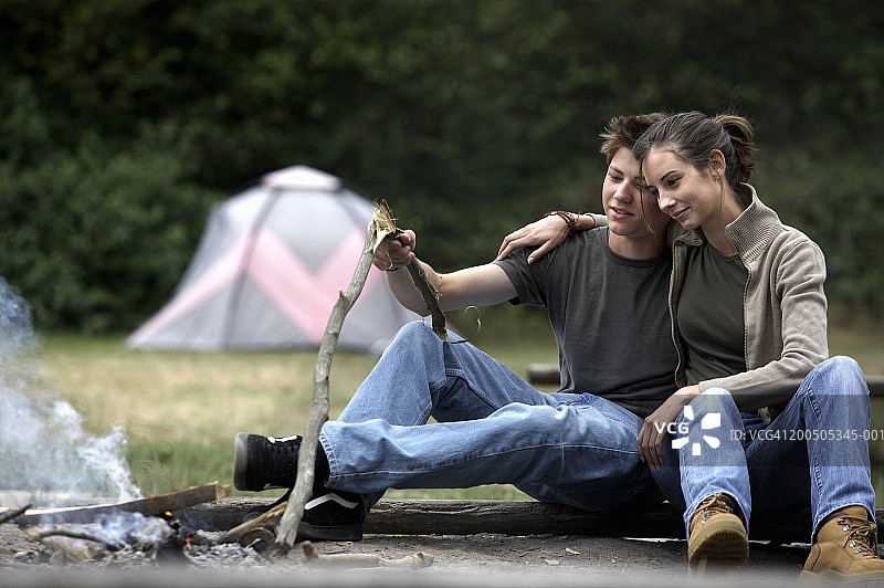 一对年轻夫妇在篝火旁拥抱，背景是帐篷图片素材