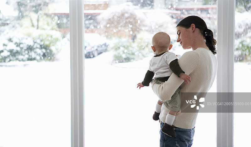 母亲和婴儿(3-6个月)望着窗外的雪图片素材