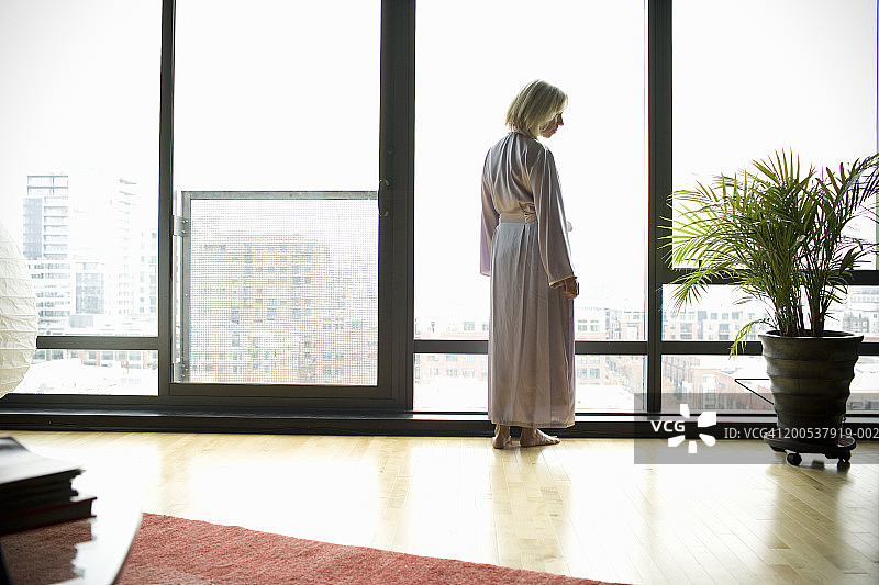 成熟的女人穿着浴袍站在客厅，后视镜图片素材