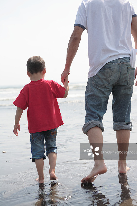 父亲和儿子(4-5)走在海滩上，后视图图片素材