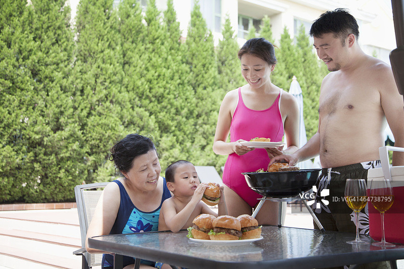 微笑的多代家庭烧烤在游泳池度假图片素材