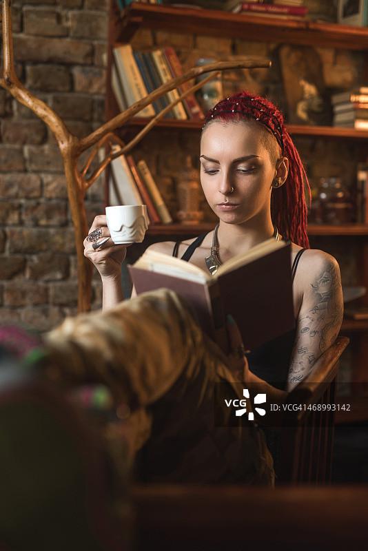一个梳着脏辫的女人在咖啡馆里看书。图片素材