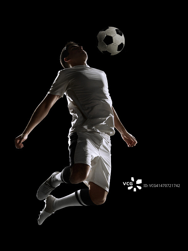 在黑色背景下的体育场中踢球的足球运动员图片素材