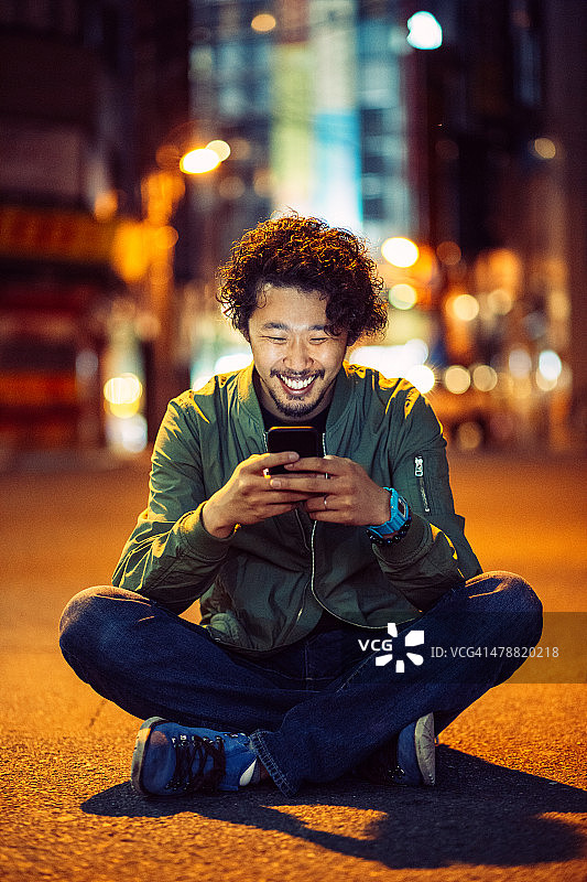 一名年轻的日本少年晚上在户外拿着手机微笑图片素材