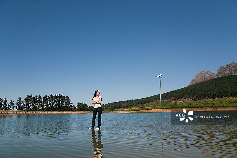 一个站在水上的女人带着监控摄像头和树图片素材