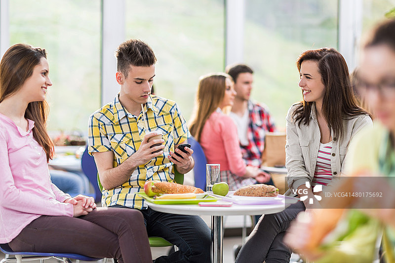 快乐的学生在食堂的午餐休息时间交流。图片素材