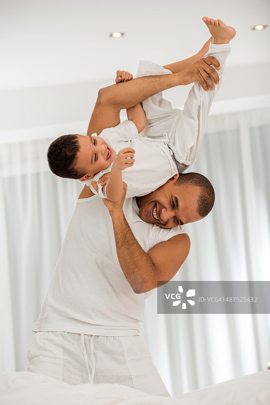 快乐的非裔美国父亲和儿子在卧室里玩耍。图片素材
