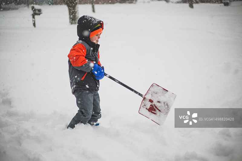 小男孩用一把小铲子铲雪图片素材