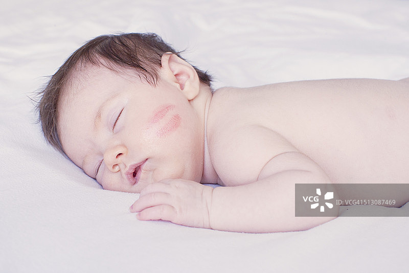 宝宝在床上打盹，脸颊上有唇印图片素材