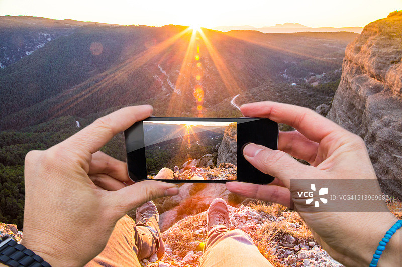 在加泰罗尼亚比利牛斯山脉，一名男子用智能手机从个人角度拍摄日落美景。图片素材