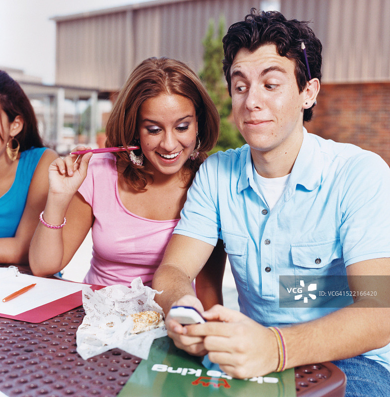 男学生和女学生坐在桌子上看手机图片素材