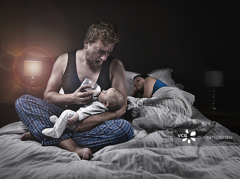 父亲用奶瓶喂养婴儿(1-6个月)，而母亲睡觉图片素材