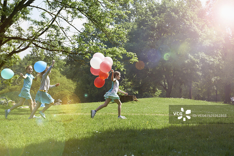 Girls running in park with balloons, Munich, Bavaria, Germany图片素材