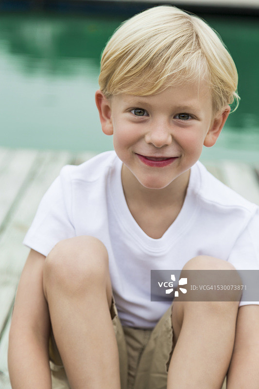 微笑的小男孩坐在码头上的肖像图片素材