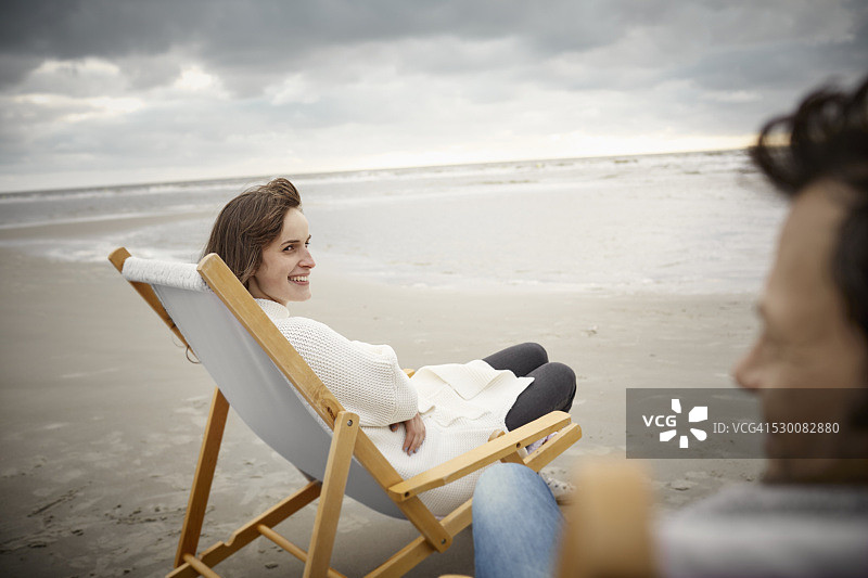 年轻的女人和男人在沙滩上的躺椅上放松图片素材