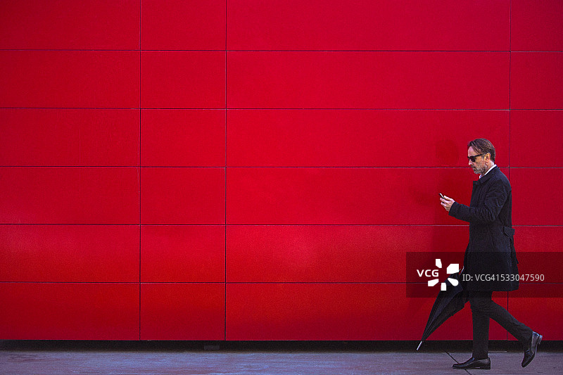 身着黑衣的英俊男子走在红墙旁图片素材
