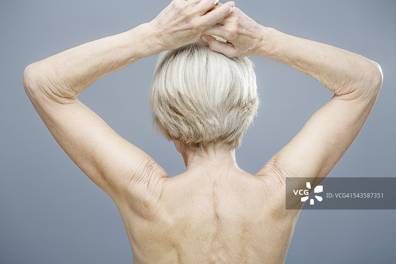 年长女性举起手臂的背影。图片素材