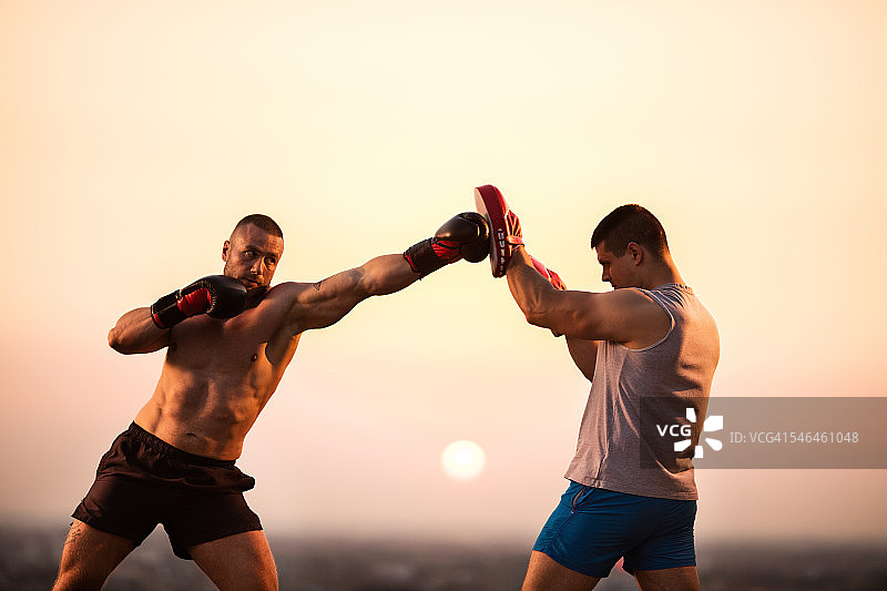 强壮的拳击手在日落和他的私人教练锻炼。图片素材