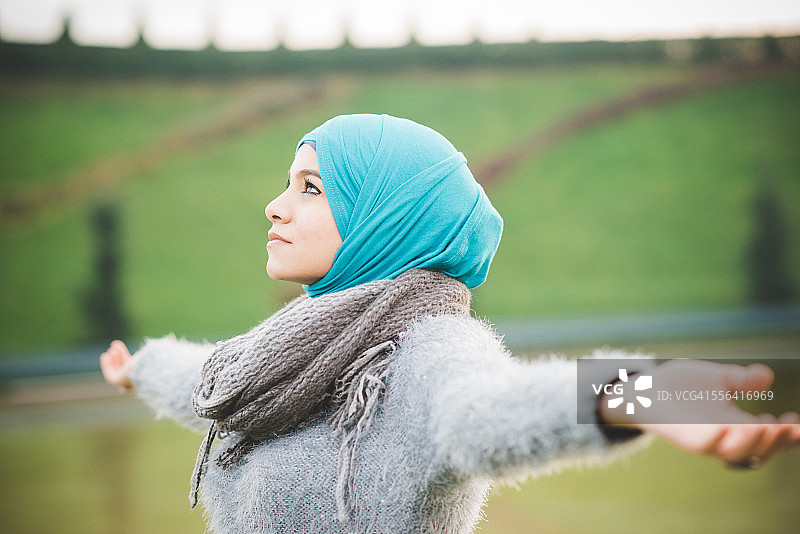 公园里的年轻女子张开双臂，戴着蓝绿色的头巾图片素材