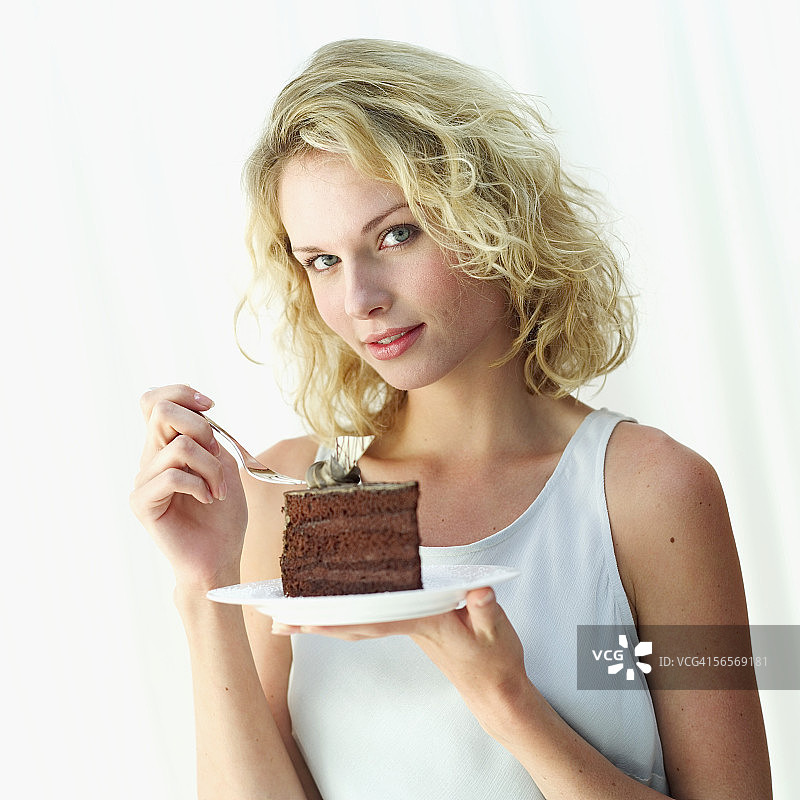 一个年轻女子的肖像，手里拿着一块放在盘子里的巧克力蛋糕图片素材