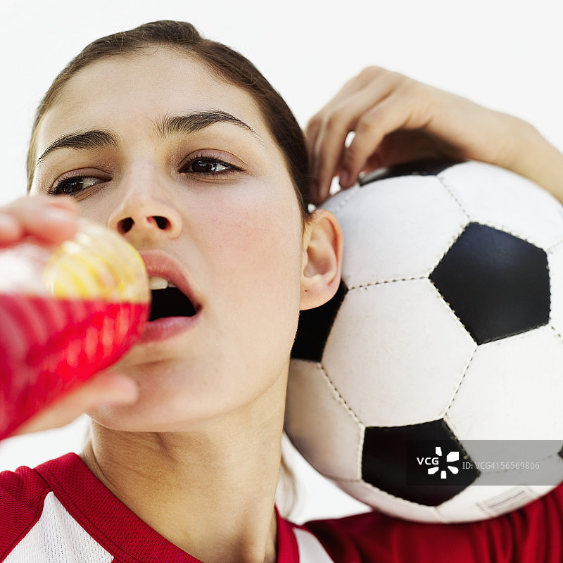 一个年轻女子拿着一个足球，从瓶子里喝水图片素材