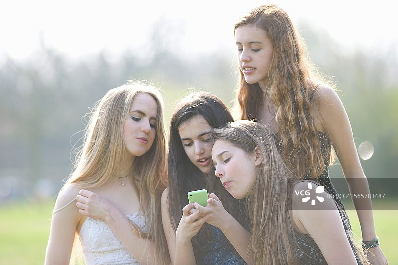 四个十几岁的女孩在公园里看手机短信图片素材