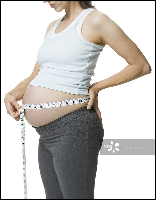 一名孕妇用卷尺测量她的腹部的中段视图图片素材