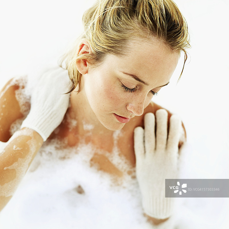 年轻女子戴着丝瓜络手套洗泡泡浴图片素材