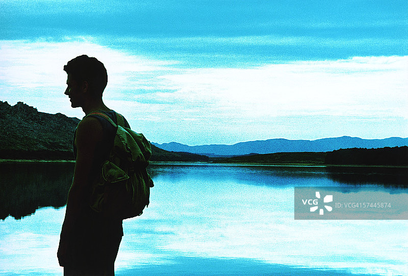 一个背着背包的年轻人站在湖边的侧面照片图片素材