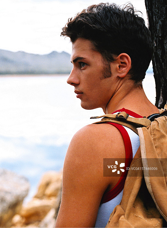 侧面特写的一个年轻男子背着一个背包看着湖面图片素材