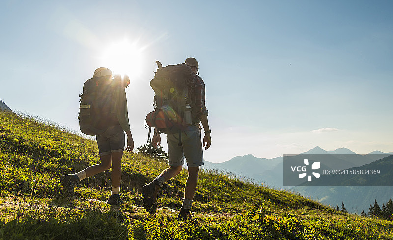 奥地利，蒂罗尔，坦海默·塔尔，一对年轻夫妇在背光下徒步在高山草地上图片素材