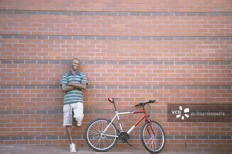 一个骑着山地车靠砖墙站着的男人图片素材