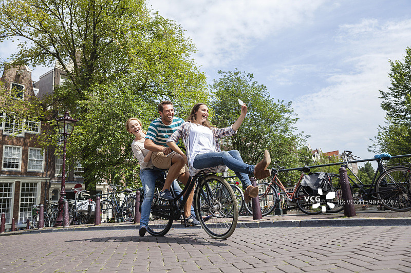 荷兰，阿姆斯特丹，三个好玩的朋友骑着一辆自行车在城市里图片素材
