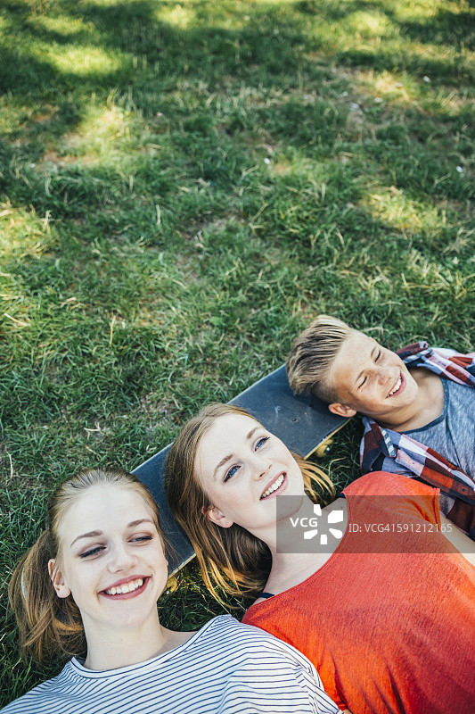 三个快乐的青少年朋友躺在滑板上在草地图片素材