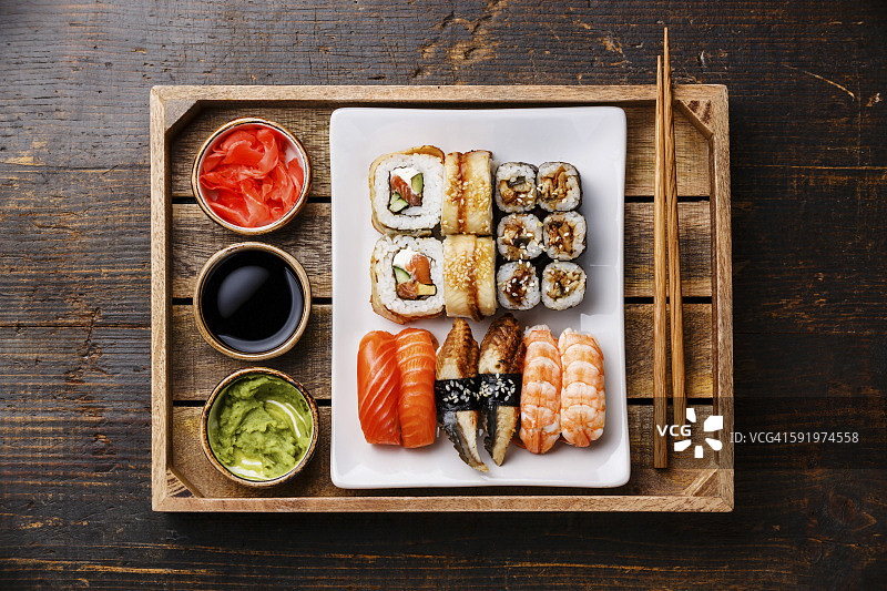 寿司将手握寿司、寿司卷、筷子、生姜、酱油和芥末放在托盘中，放置在质朴的木质背景上图片素材