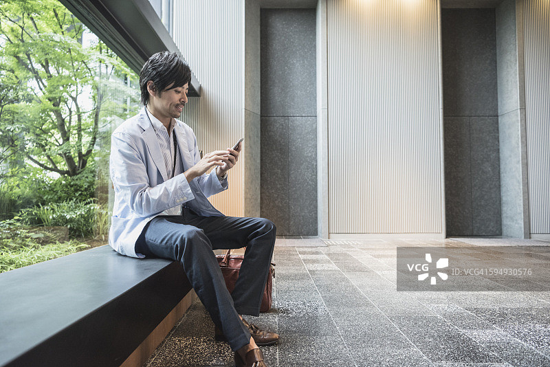 一名日本男子坐在长凳上玩手机图片素材