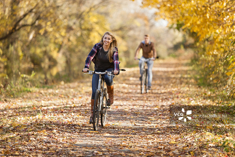 一个十几岁的男孩和一个成年的姐姐在秋天的森林里骑车图片素材